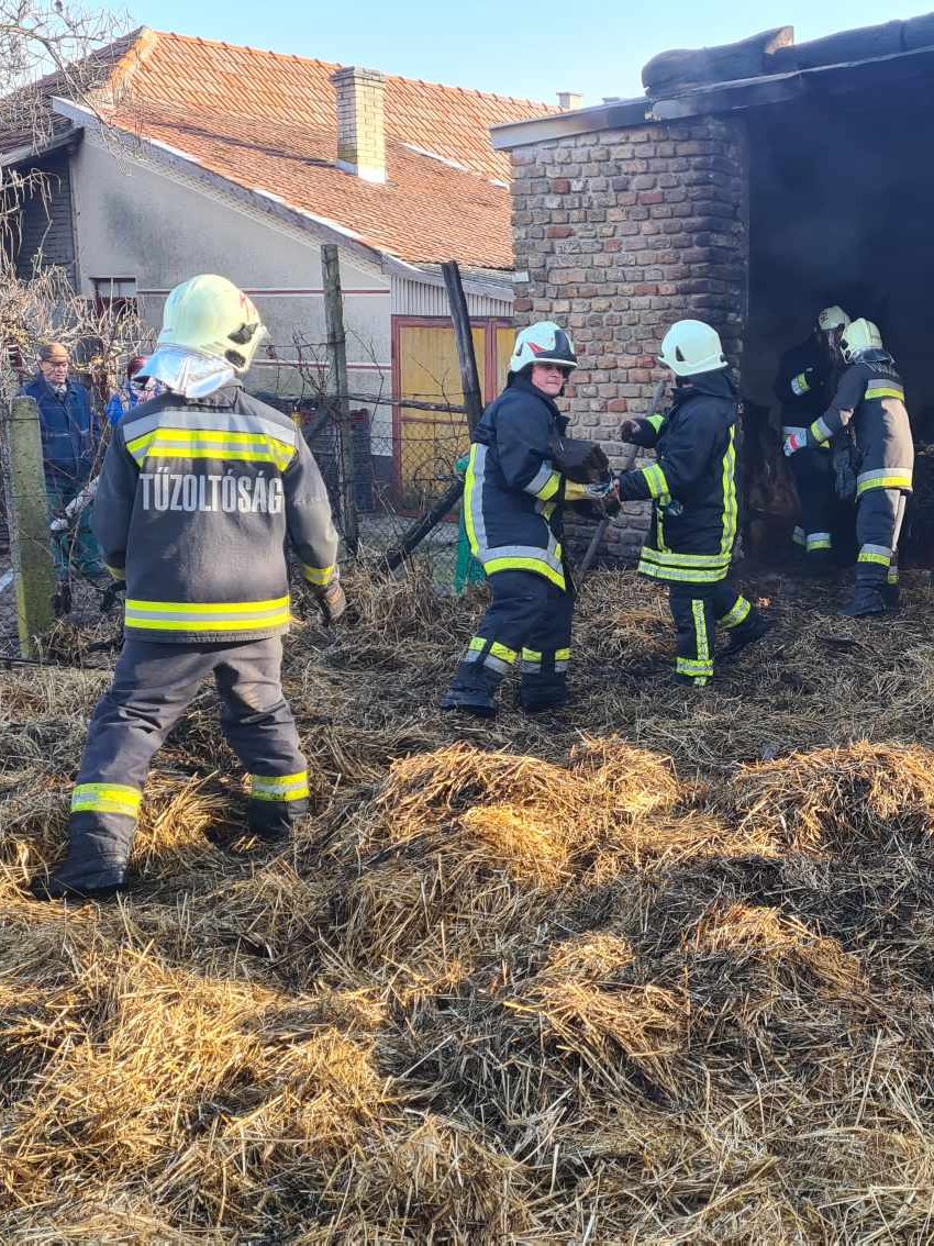 Öt tagunk teljes védőfelszerelésben, sisakban dolgozik egy kiégett melléképület előtt, a szalma szétbontásán.