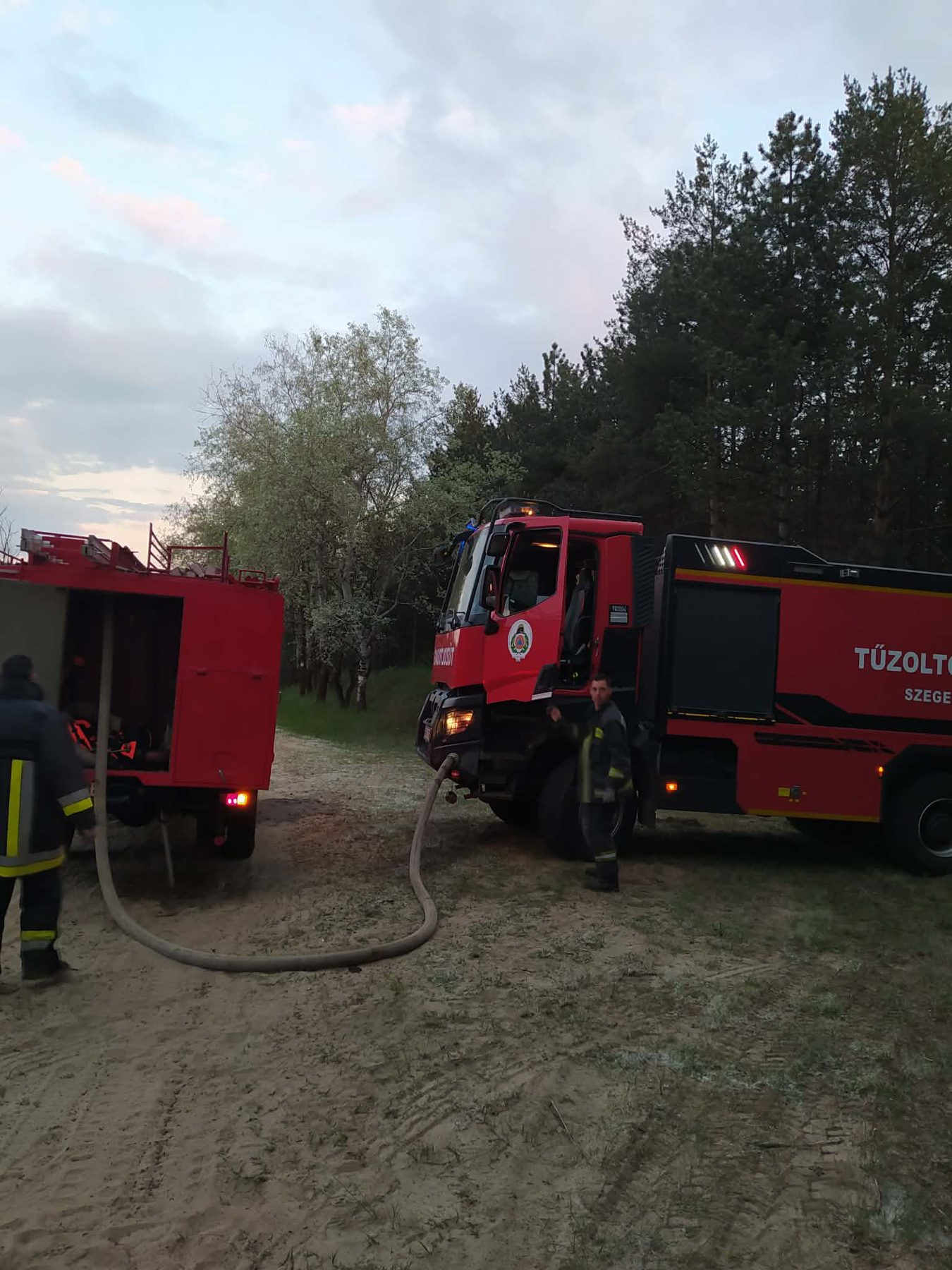 A Magirus és a hivatásos őrs modern tűzoltóautója egy erdei homokúton, köztük tömlő.